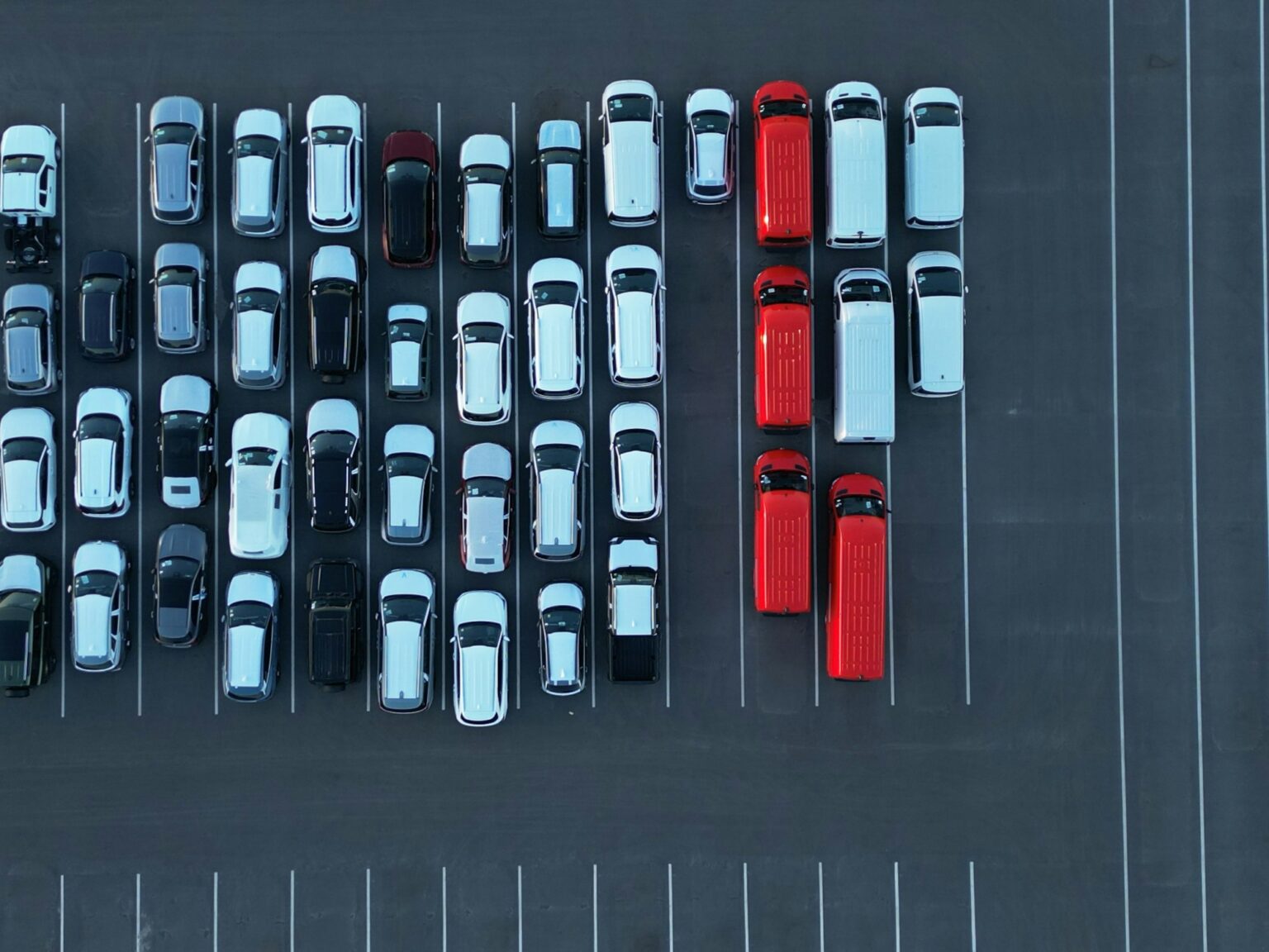 Aerial view of a business fleet lot with rows of white vehicles and a line of red vans